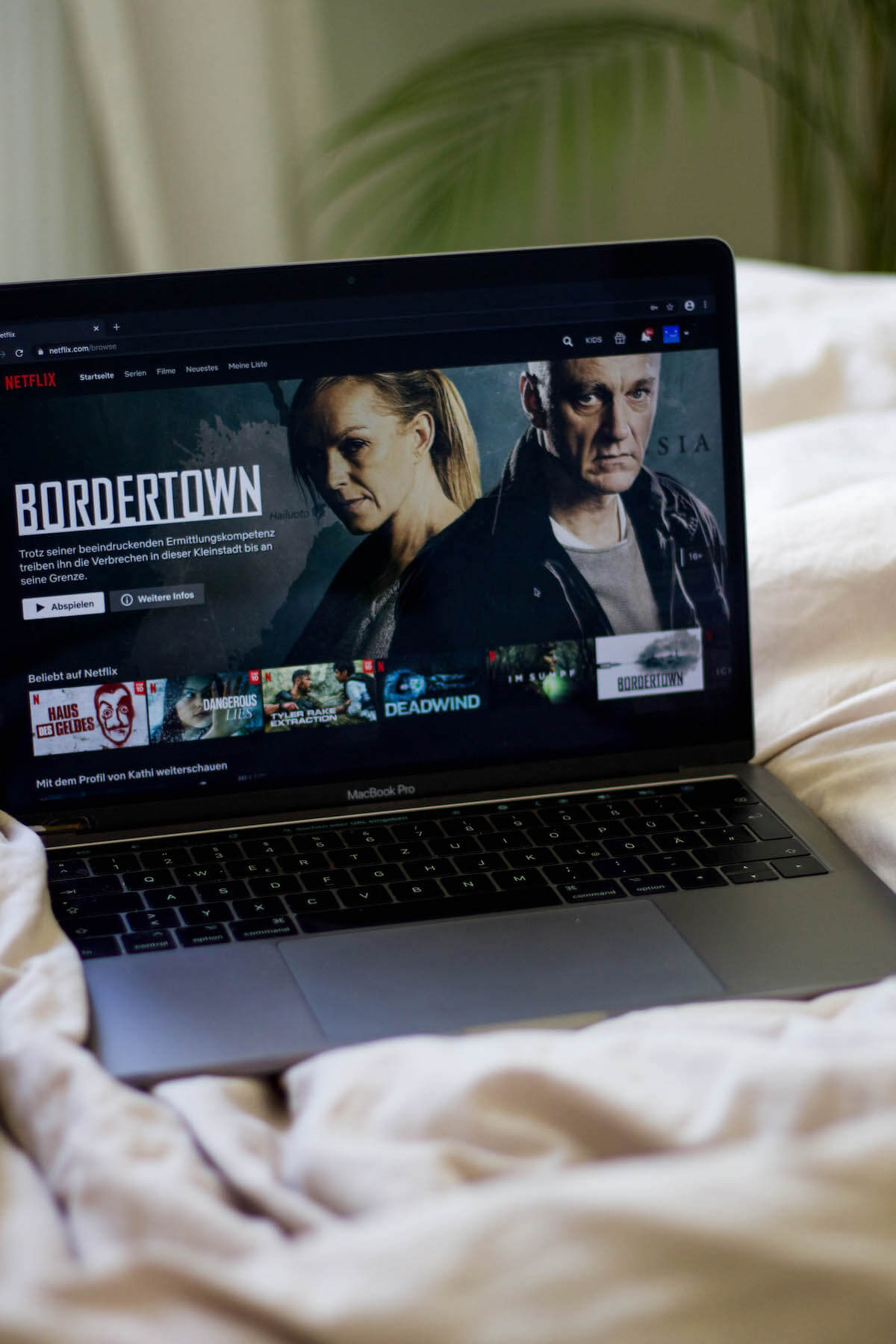 Laptop, der in einem Bett liegt und auf dem gerade Netflix läuft 