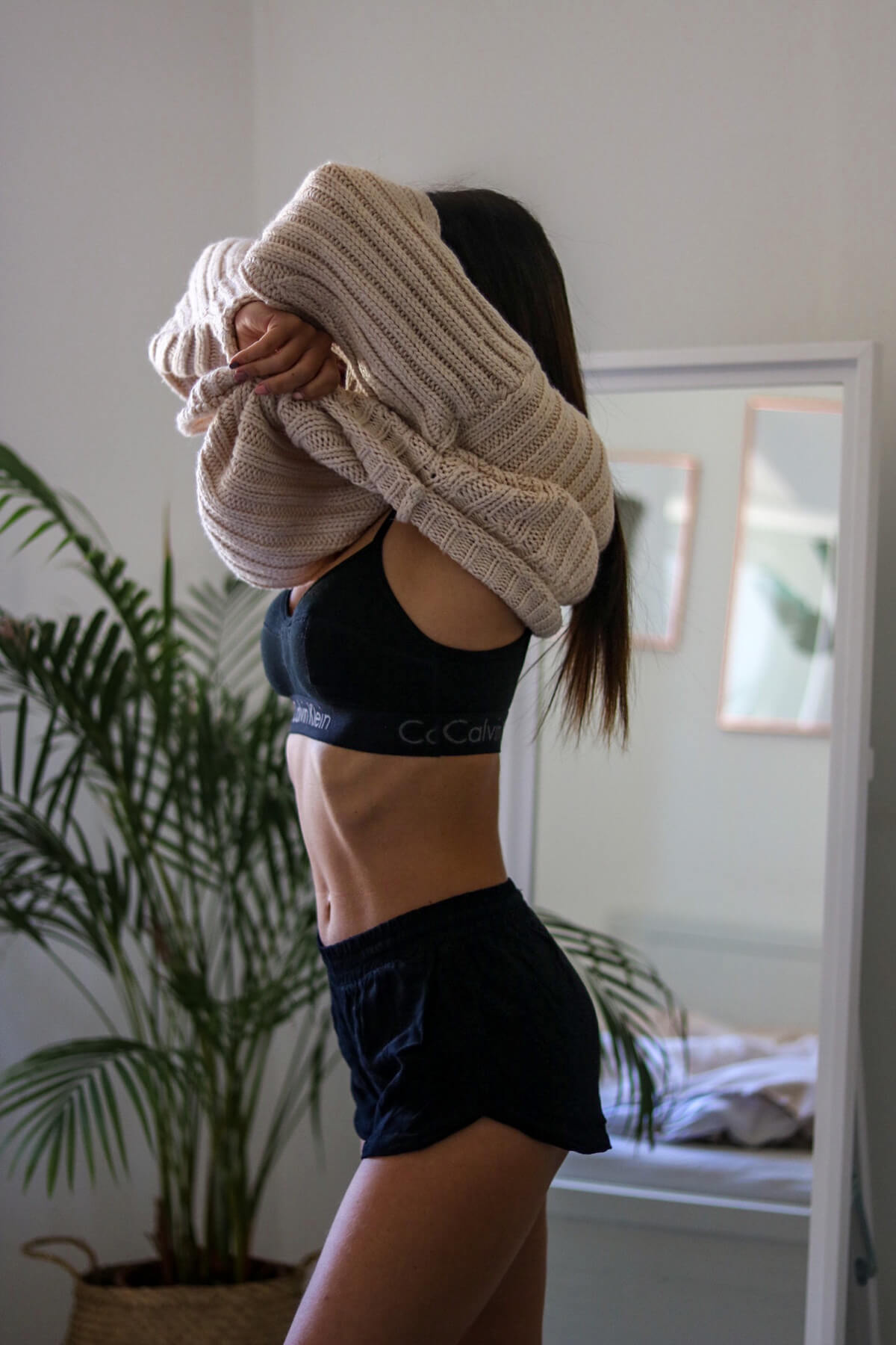 Junge Frau in Schlafzimmer, die sich gerne ihren Pullover auszieht